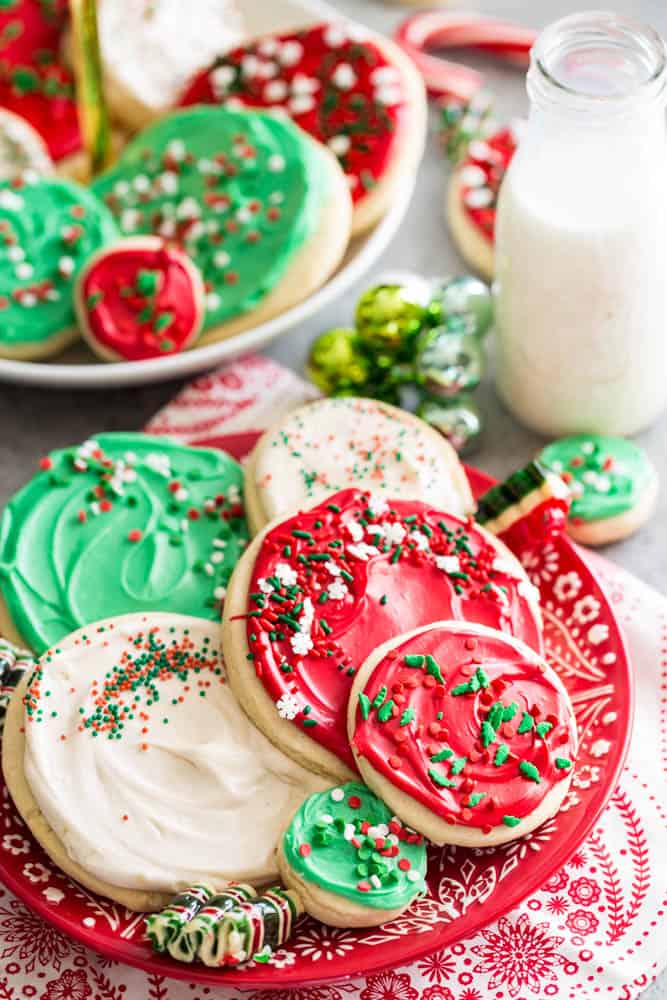 Red, green, and white cookies on a red and white cake plate with a dish towel underneath. 
