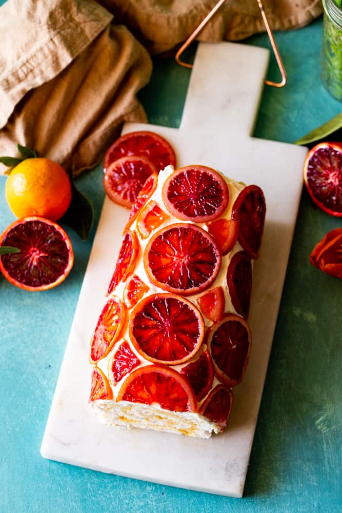 Overhead shot of the candied blood orange angel food cake roll on a white cutting board.