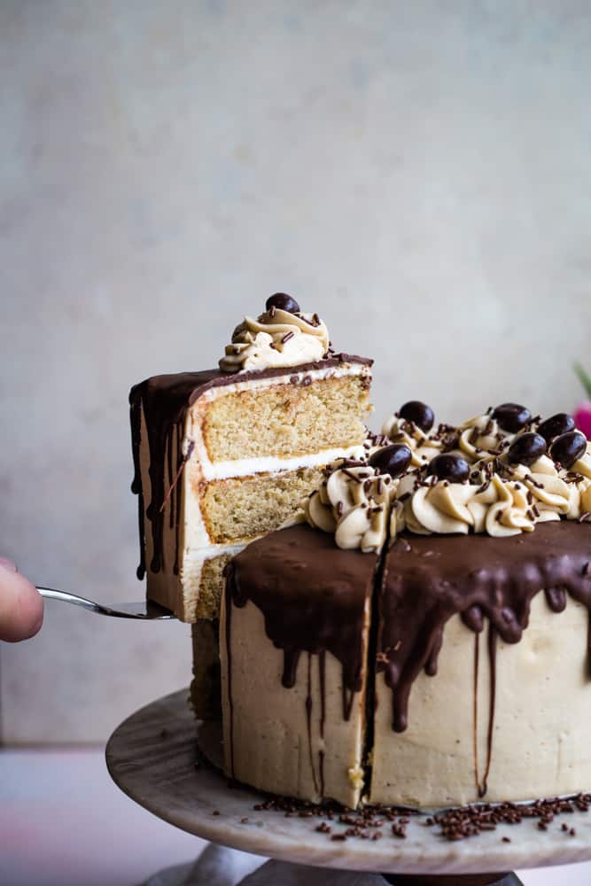 Hand using a cake knife and removing a slice of the coffee layered cake on cake stand. 