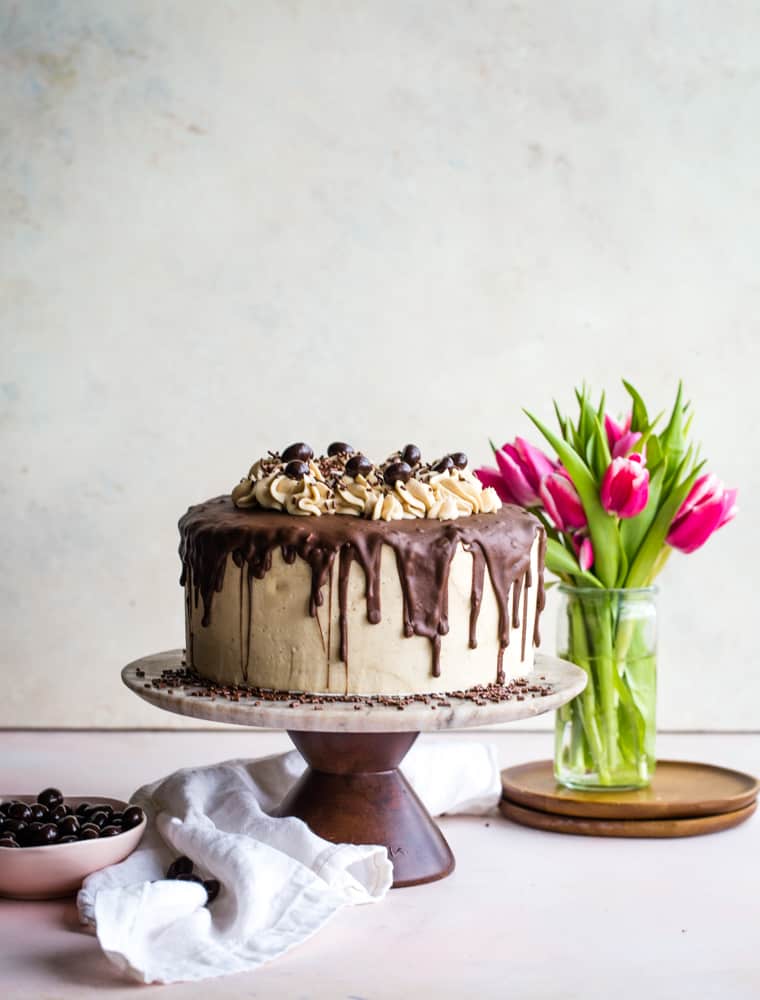Coffee Layered Cake with Mascarpone Frosting on a marble cake plate with fresh hot pink tulips in the background. 