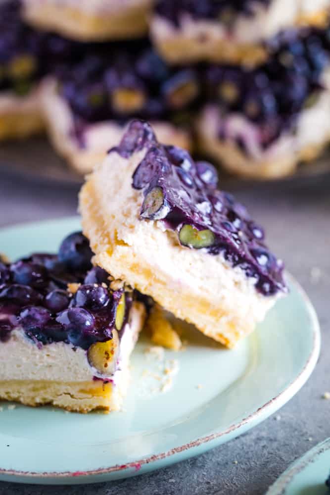 Two cut blueberry bars leaning on each other on a pale teal plate. 