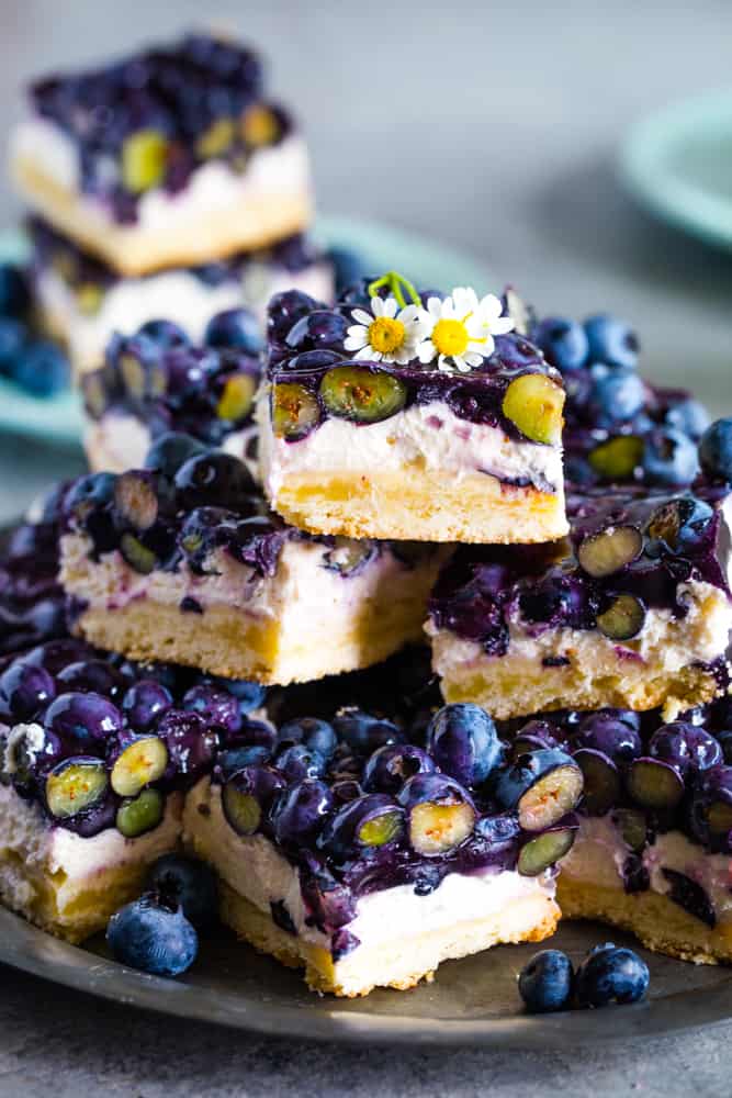 Blueberry Cream Cheese Bars stacked on a metal plate with fresh berries all around. 