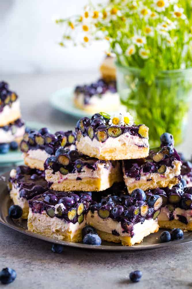 Blueberry Cream Cheese Bars cut into squares and layered on a metal plate with fresh berries around them. 