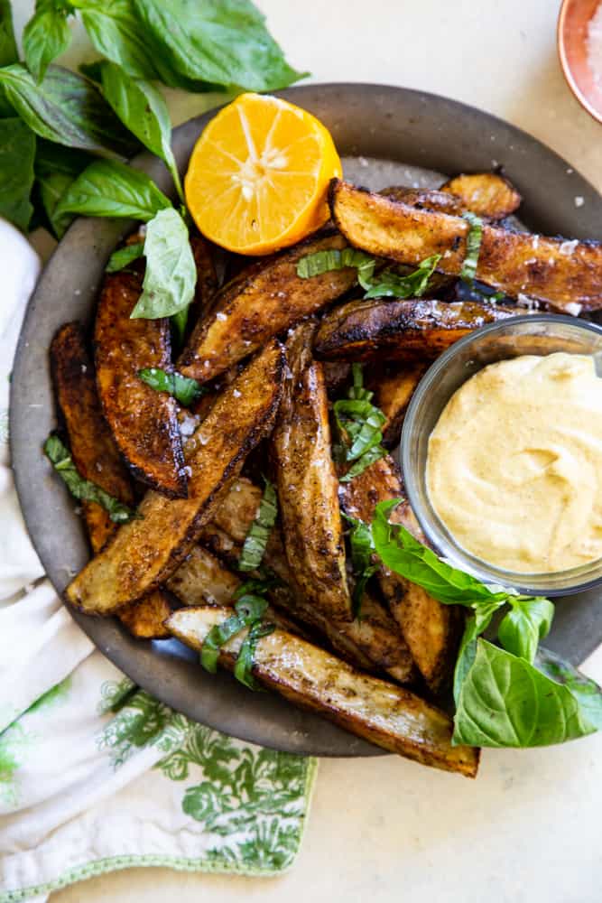 Crispy Pesto Potato Wedges on a metal plate with basil and a cut lemon next to them. 