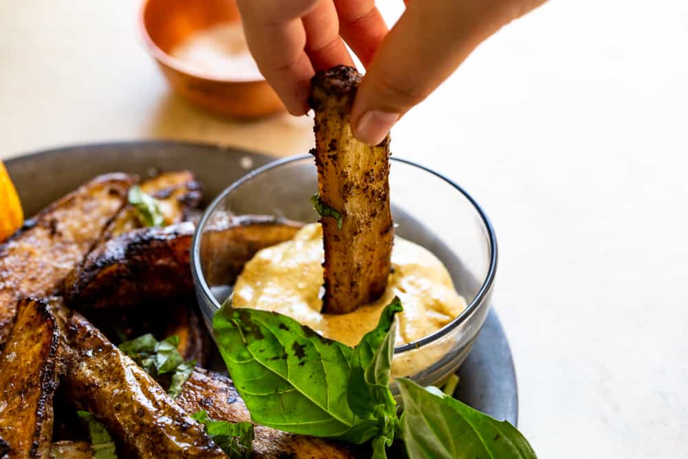 Hand dipping potato wedge into small bowl of the aioli. 