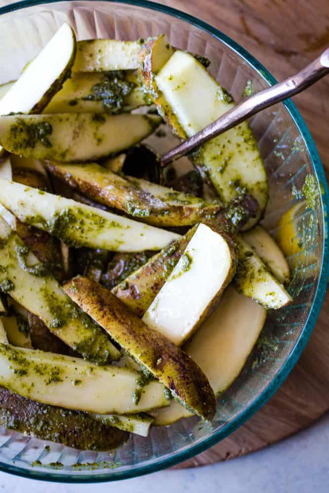 Tossing the raw potato wedges with the fresh pesto sauce in bowl. 