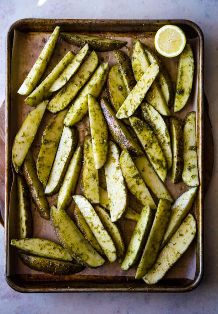 Overhead shot of uncooked potato wedges with pesto on a parchment lined pan. 