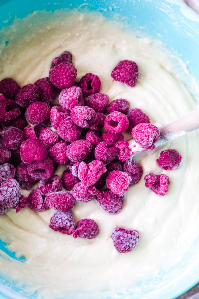 Pound cake batter in blue bowl with fresh raspberries being stirred in. 