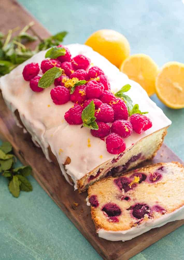 Pound Cake with fresh raspberries, mint leaves, and lemon slices on a wood cutting board. 