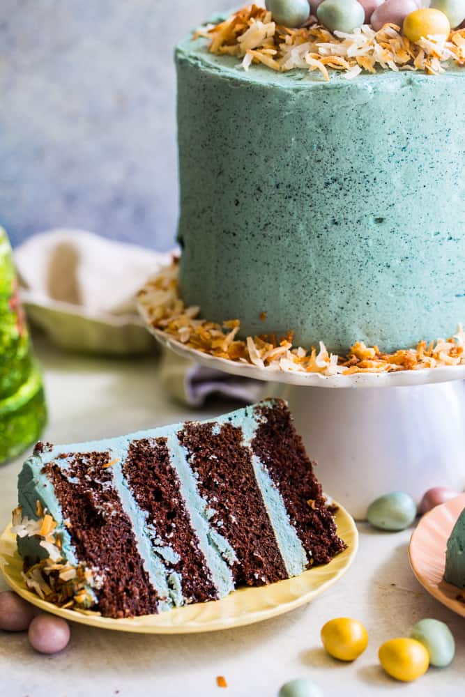 Slice of 4 layer cake on a small yellow plate with full cake in background on white plate. 