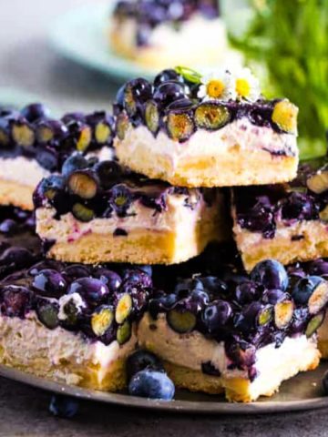 Stacked blueberry cream cheese bars on a metal plate with green bouquet in background.