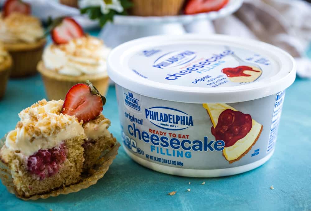 Philadelphia cheesecake filling tub next to the cut in half cupcake. 