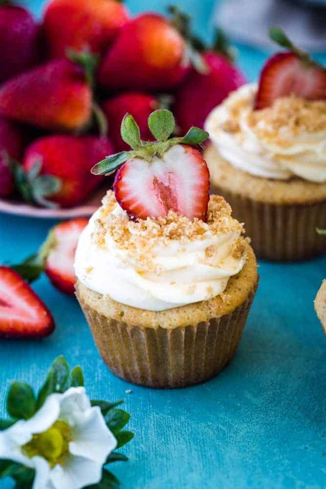 cupcake with fresh cut strawberry and frosting on blue background with plate of strawberries. 