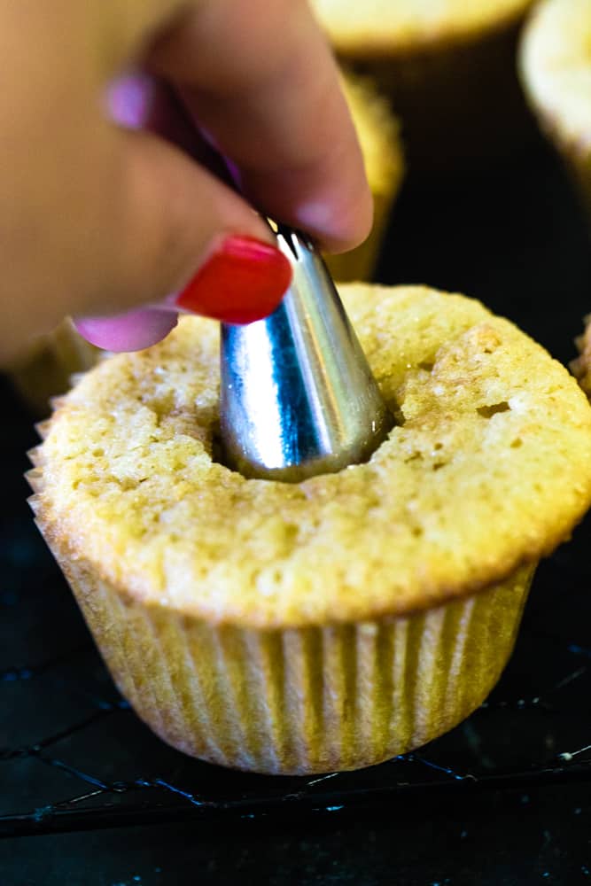 Hand using the back of a large frosting tip to cut hole in cupcake