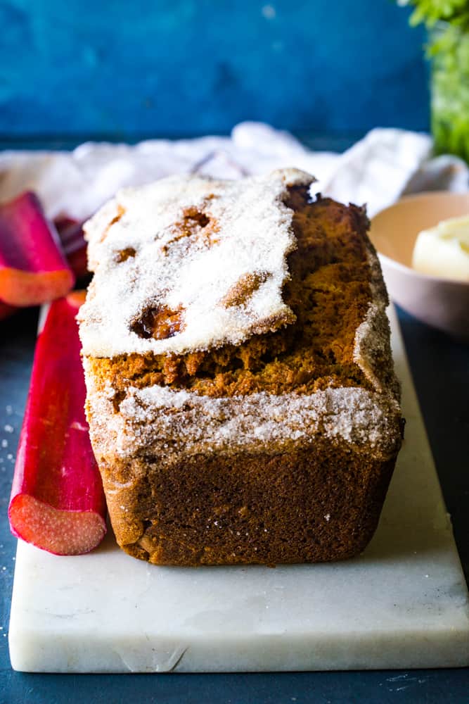 whole rhubarb streusel bread that uncut on a white tray with fresh rhubarb stalks next to it. 