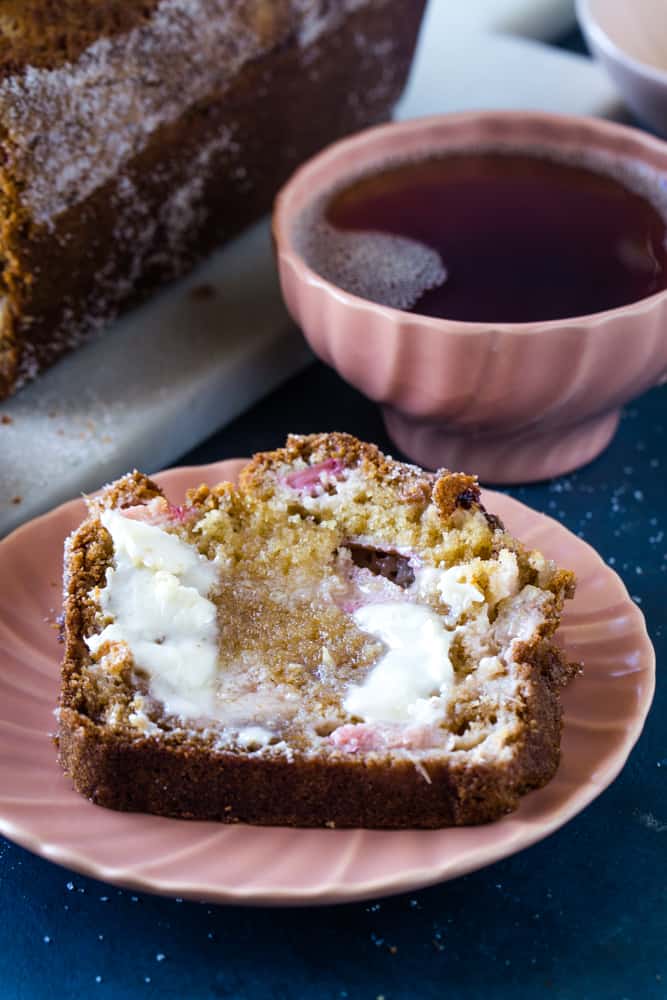 slice of rhubarb streusel bread on pink plate with a cup of tea next to it. 