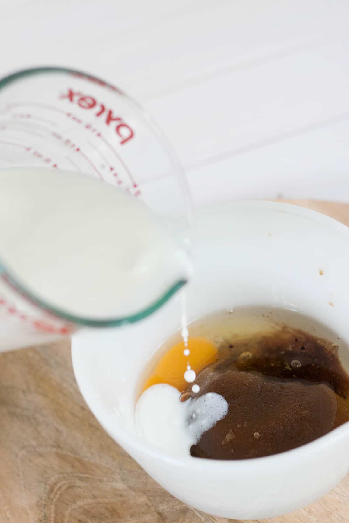 Pouring milk in a white bowl with eggs and sugar  and brown sugar. 