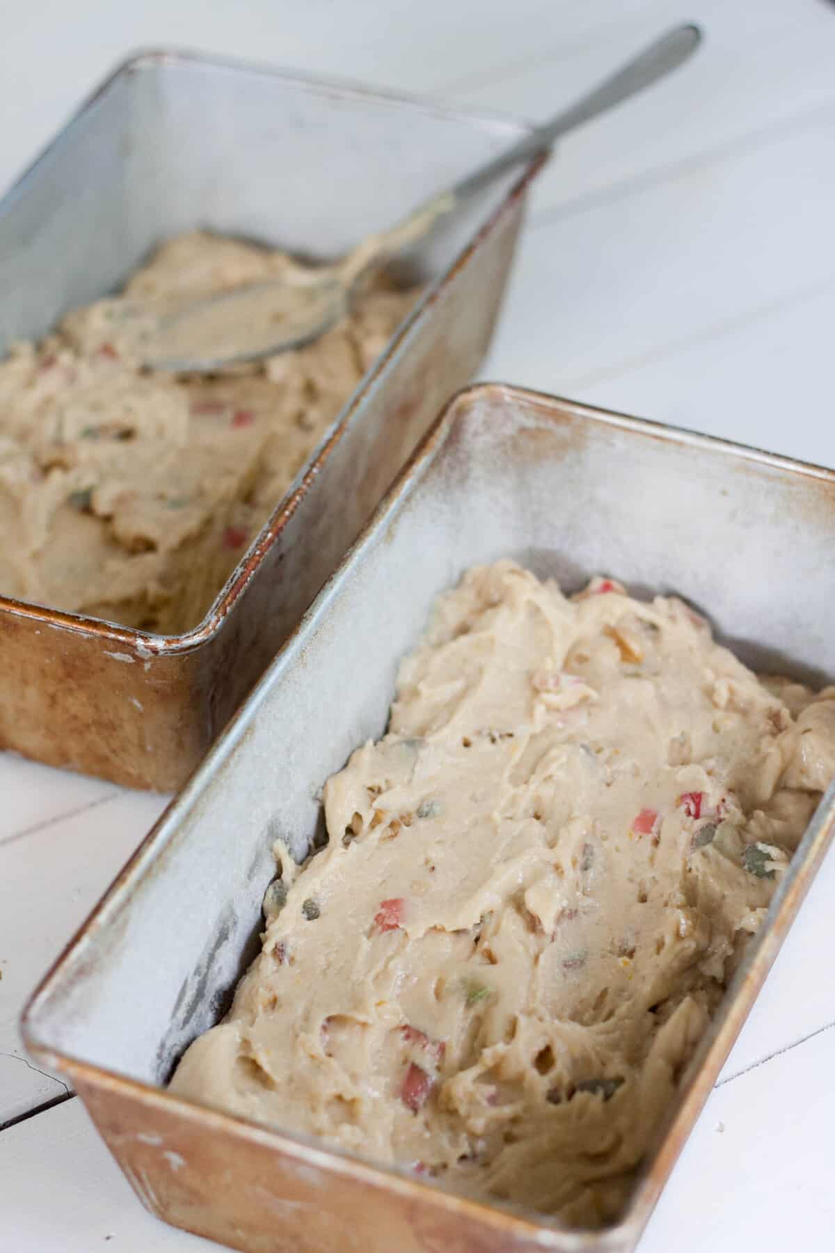 Two loaf pans of rhubarb streusel bread batter on a white background. 