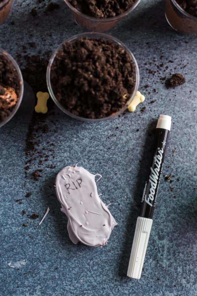 writing on the chocolate dipped tombstones for the graveyard pudding cups