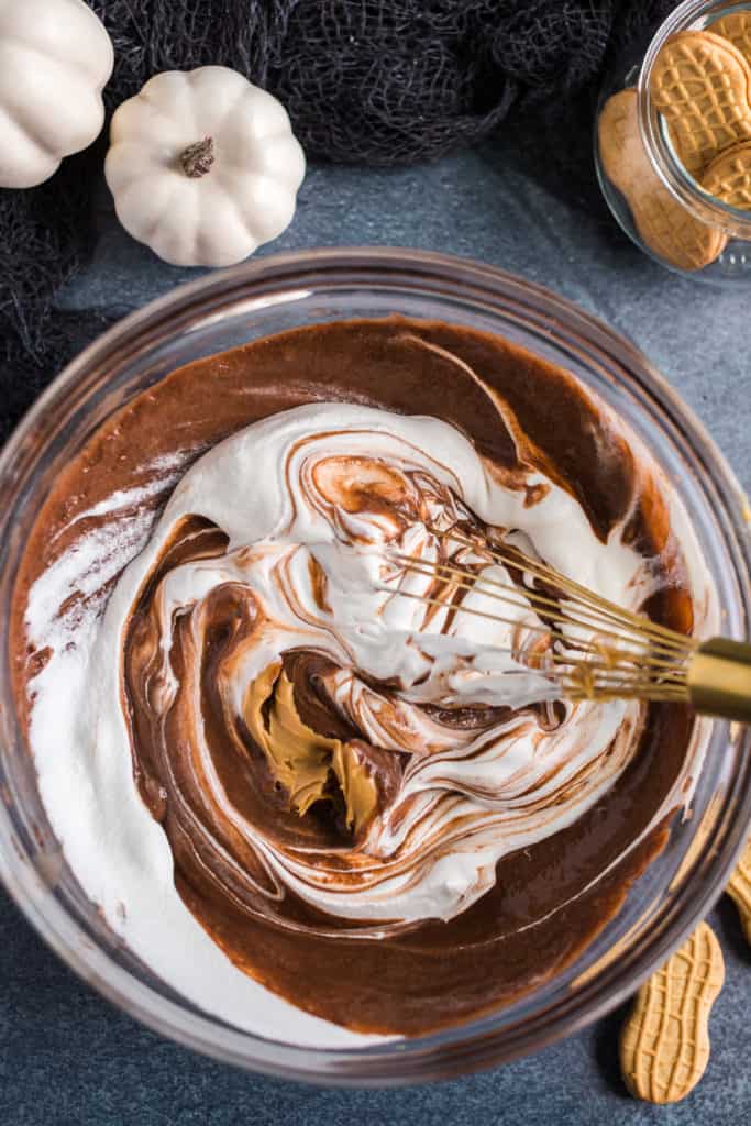 making the pudding for graveyard pudding cups by mixing peanut butter, cream, and chocolate. 