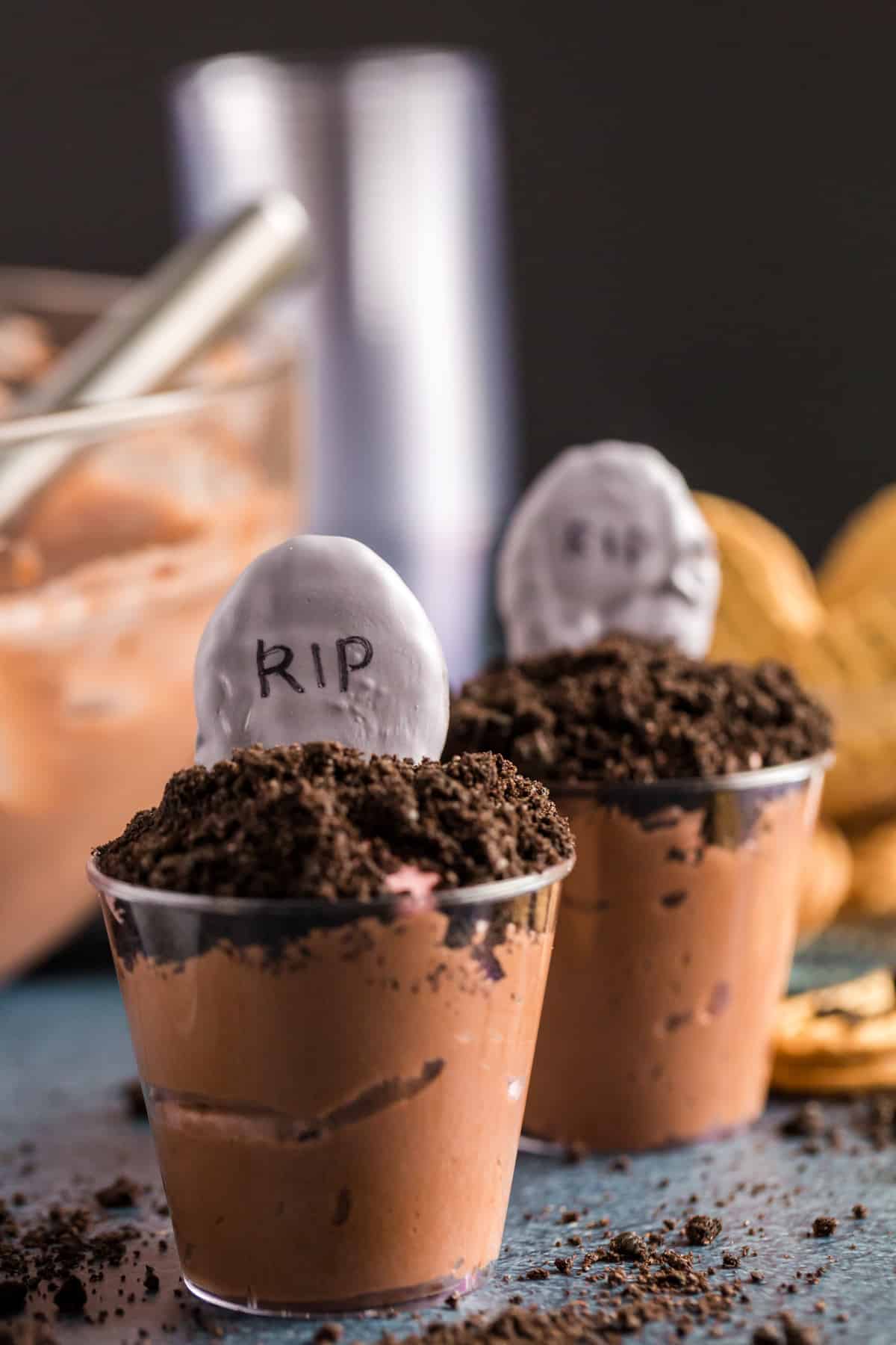 Pudding cups with cookie crumbs and a grey chocolate covered tombstone. 