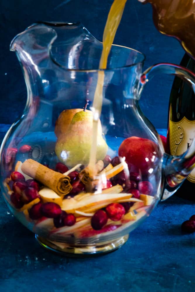 pouring champagne into pitcher filled with fruit