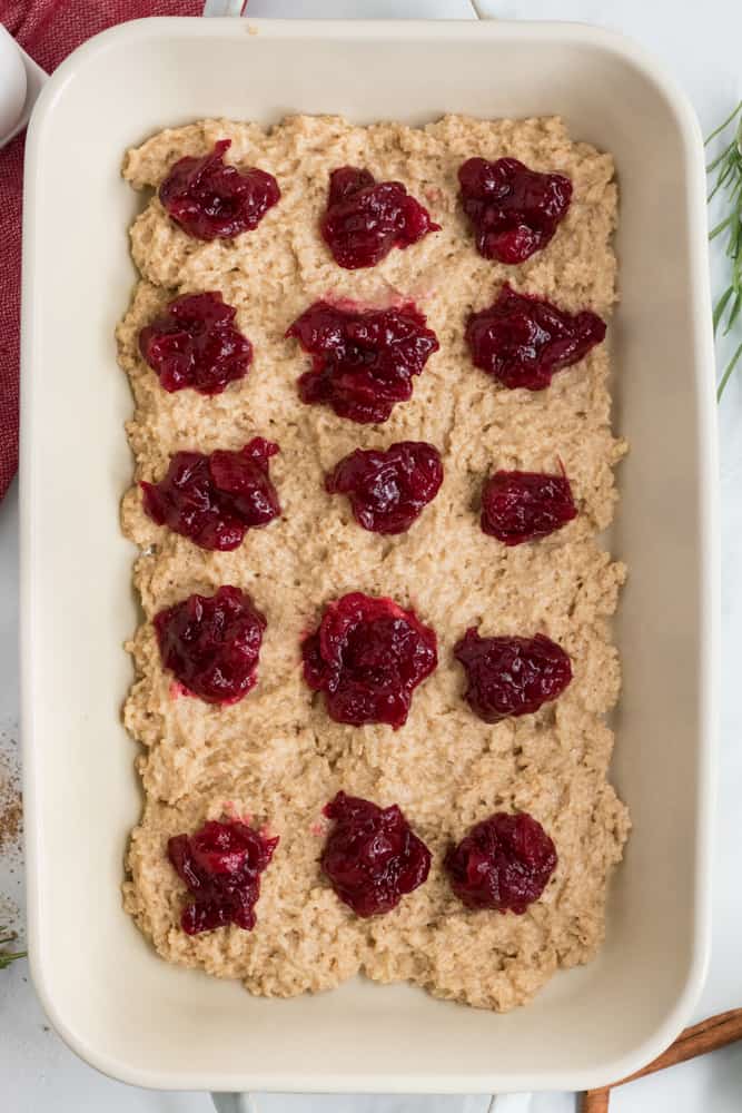 dollops of cranberry sauce over coffee cake batter in white baking dish. 