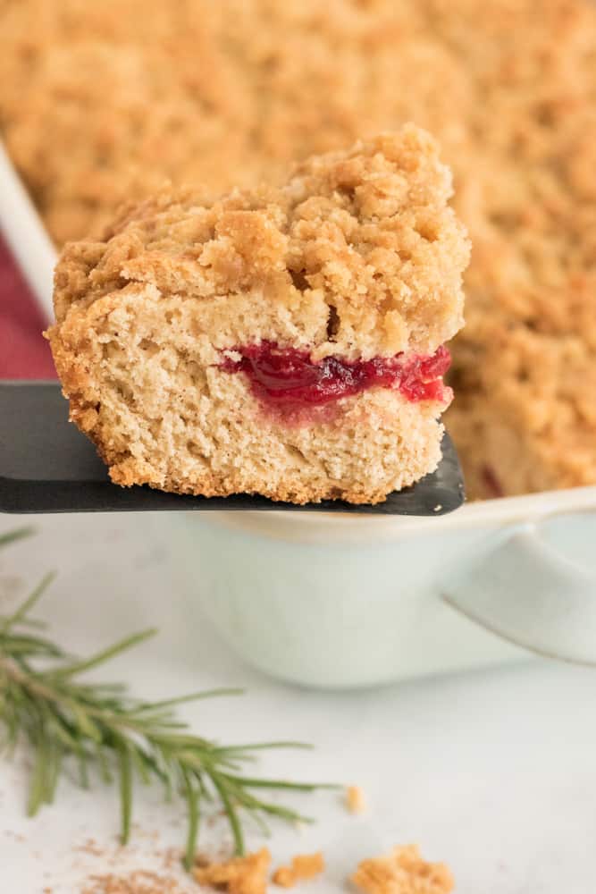 slice of cranberry sauce coffee cake on spatula being removed from white baking dish. 