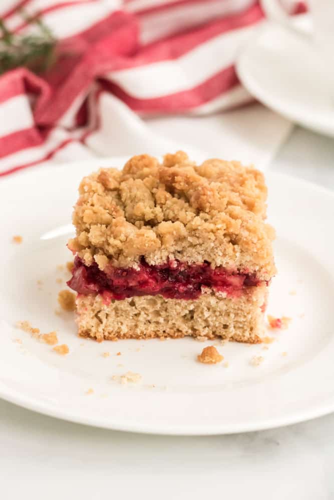 square of cranberry sauce coffee cake on white plate with red and white dish towel in background. 