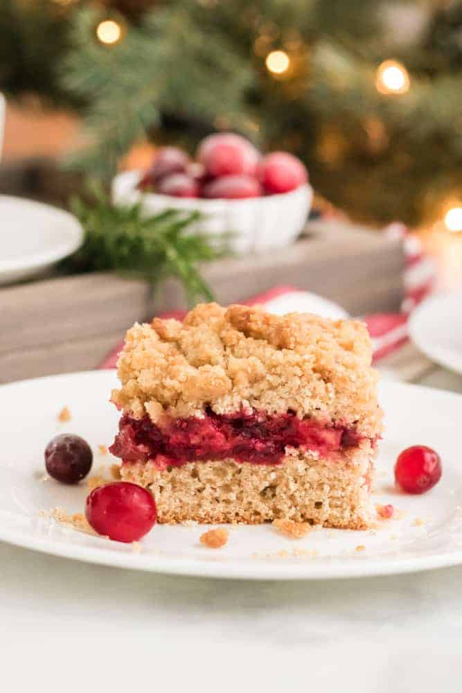 slice of cranberry sauce coffee cake on white plate with Christmas tree in the background. 