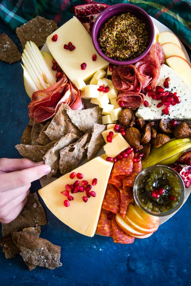 hand grabbing a buckwheat cracker on cheeseboard