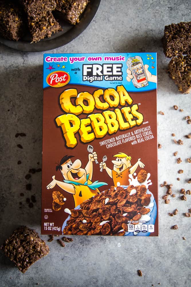 Box of cocoa pebbles cereal with Fred flinstone on the center and a plate of treats off to the side. 