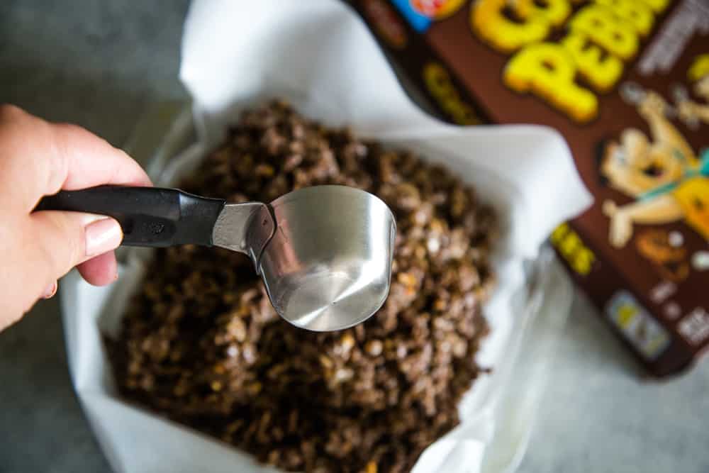 Hand holding a measuring cup for for pressing down the chocolate peanut butter squares. 