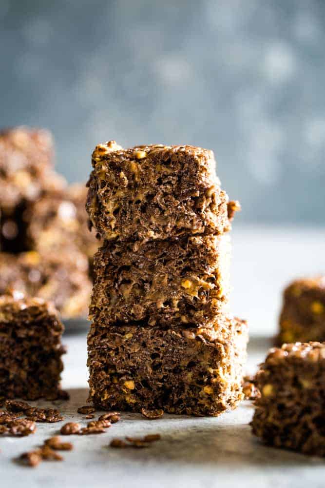 Three chocolate peanut butter squares cut and stacked on white counter with blue background. 