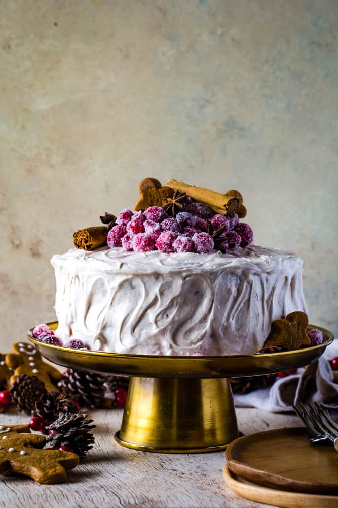 White frosted 2-layer cake on a gold metal cake plate with gingerbread cookies around it. 