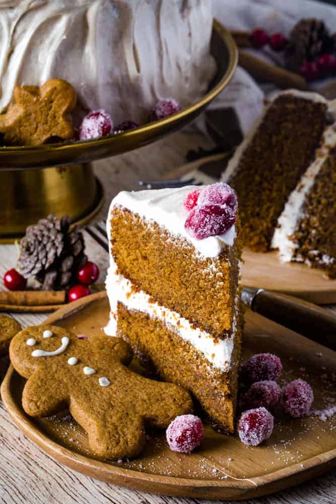 slice of gingerbread layered cake on a wood plate with gingerbread cookie next to it. 