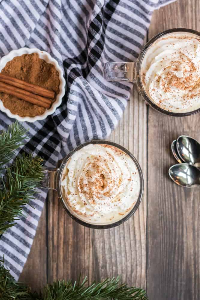 eggnog recipe topped with whipped cream and bowl of cinnamon sticks