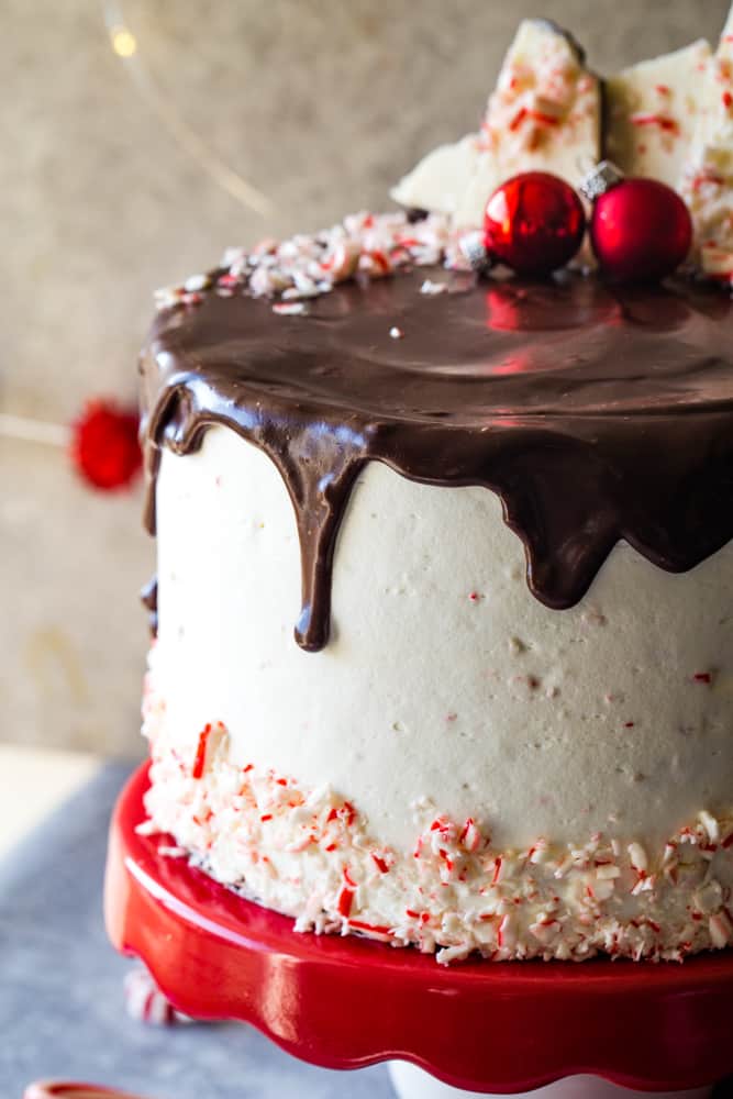Up close photo of ganache drip on the peppermint bark layer cake on red cake stand. 