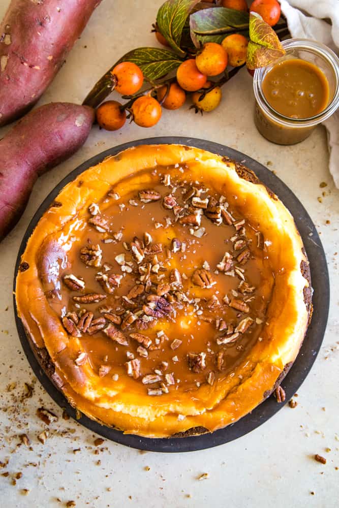 Overhead shot of whole sweet potato swirled cheesecake on metal plate with pecans. 