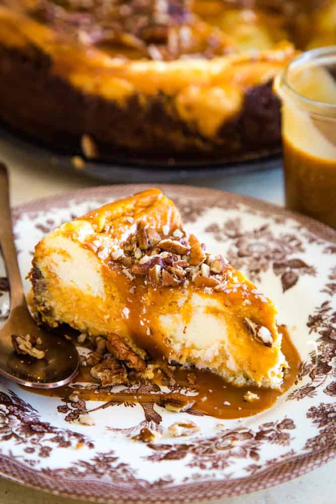 slice of sweet potato swirled cheesecake on brown plate with metal spoon and jar of caramel in the corner. 