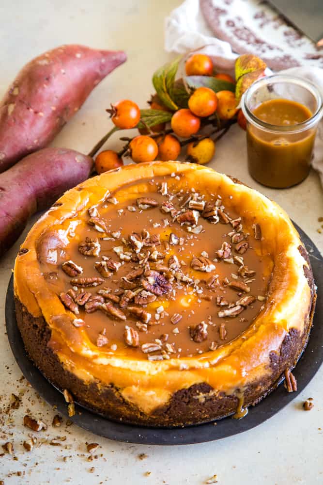 Whole sweet potato swirled cheesecake garnished with caramel drizzle and chopped pecans on a metal pie plate. 