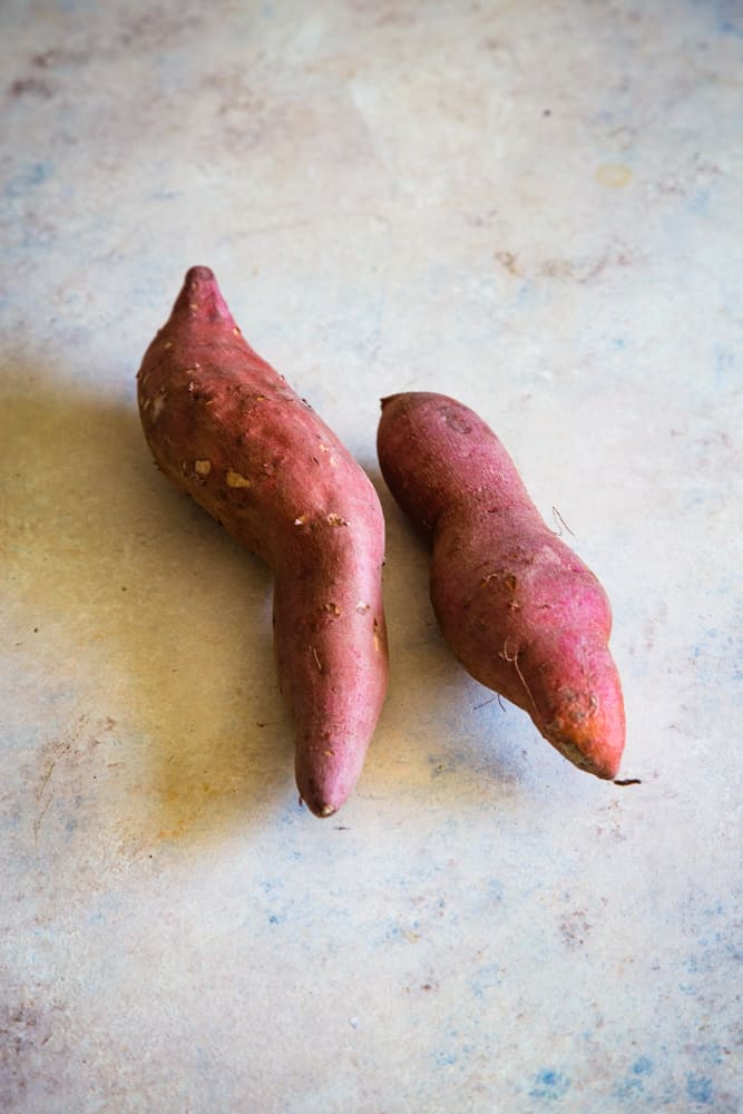 two uncooked whole sweet potatoes on a light beige background. 