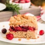 Leftover cranberry sauce coffee cake slice on small white plate with Christmas tree in background.