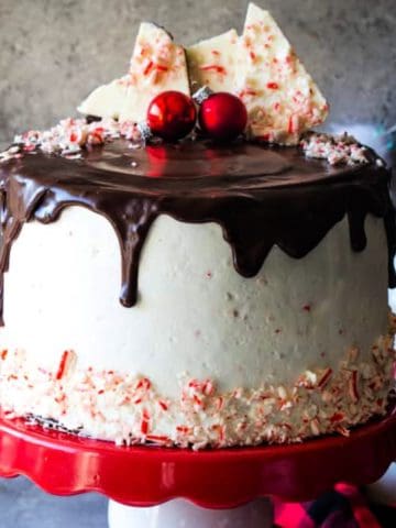 Whole peppermint bark layer cake with ganache on a red and white cake plate.