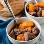 butternut squash beef stew in white bowls with spoons and bread