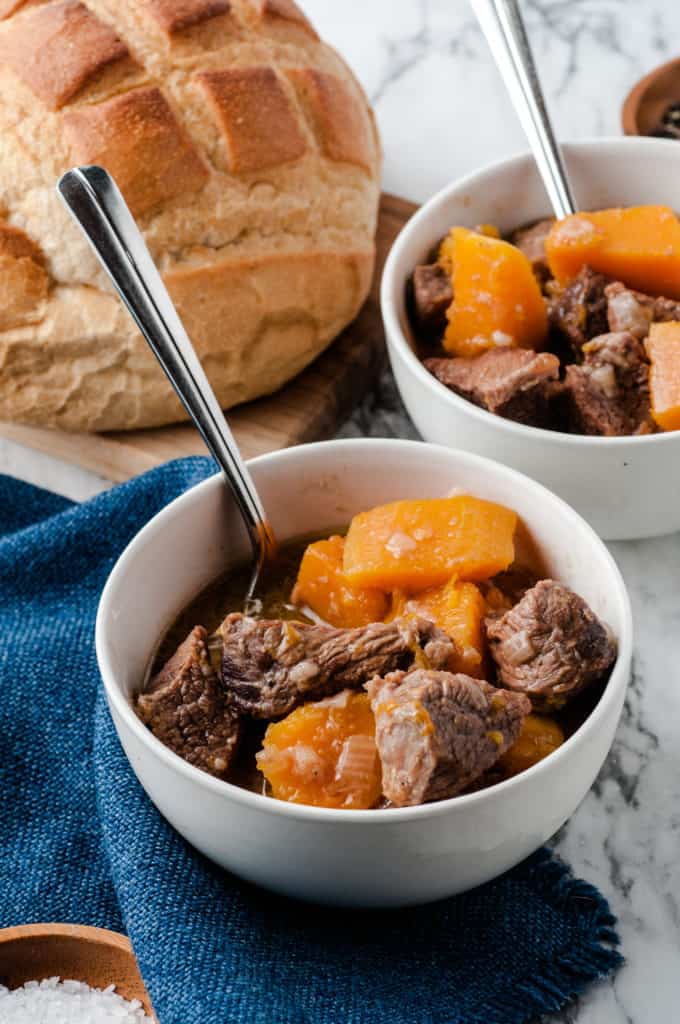 butternut squash beef stew in white bowls with spoons and bread