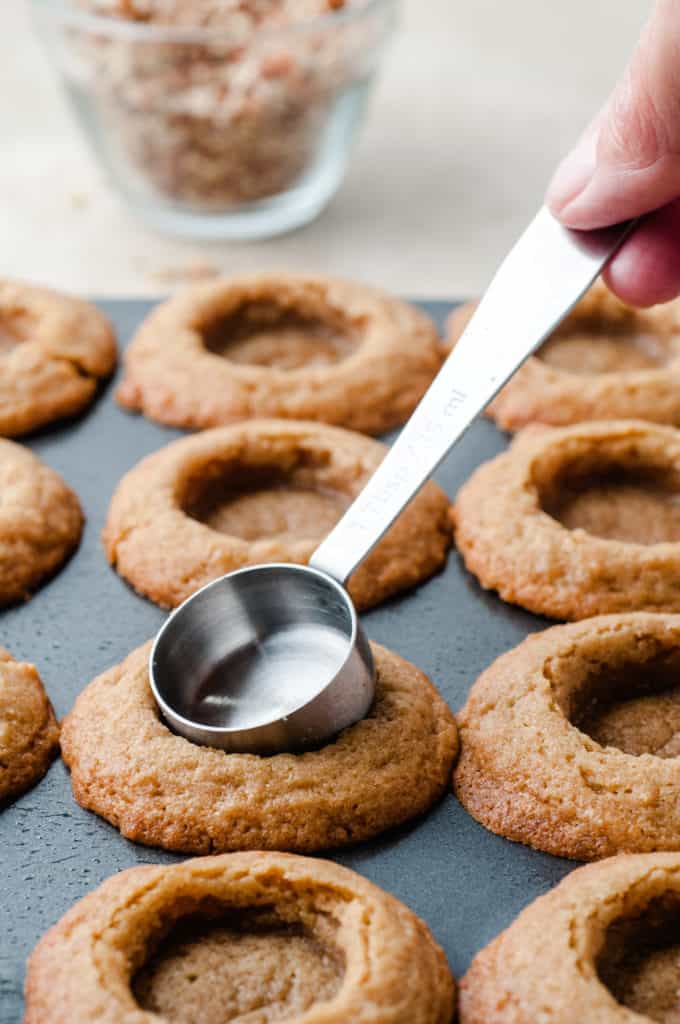 using measuring spoon to make indents in caramel pecan cookie cups