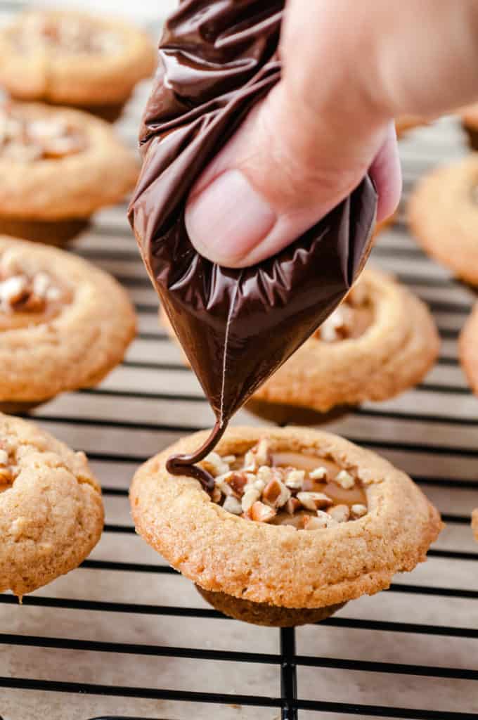 hand drizzling melted chocolate over caramel cookie cups