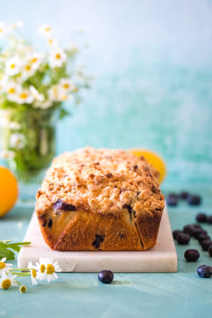 loaf of blueberry lemon streusel bread on white cutting board with flowers in the background