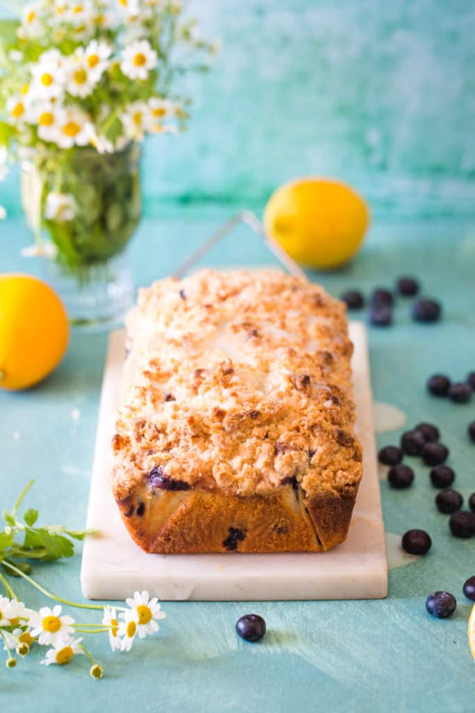 lemon blueberry loaf on white marble with flowers in background